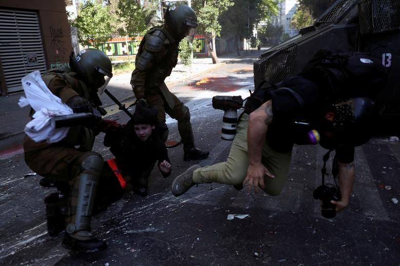A photographer falls after being pushed down by riot police, who detain a demonstrator during a protest against Chile's government, on the one-year anniversary of the protests and riots that rocked the capital in 2019, in Santiago, Chile, October 18. REUTERS/Ivan Alvarado